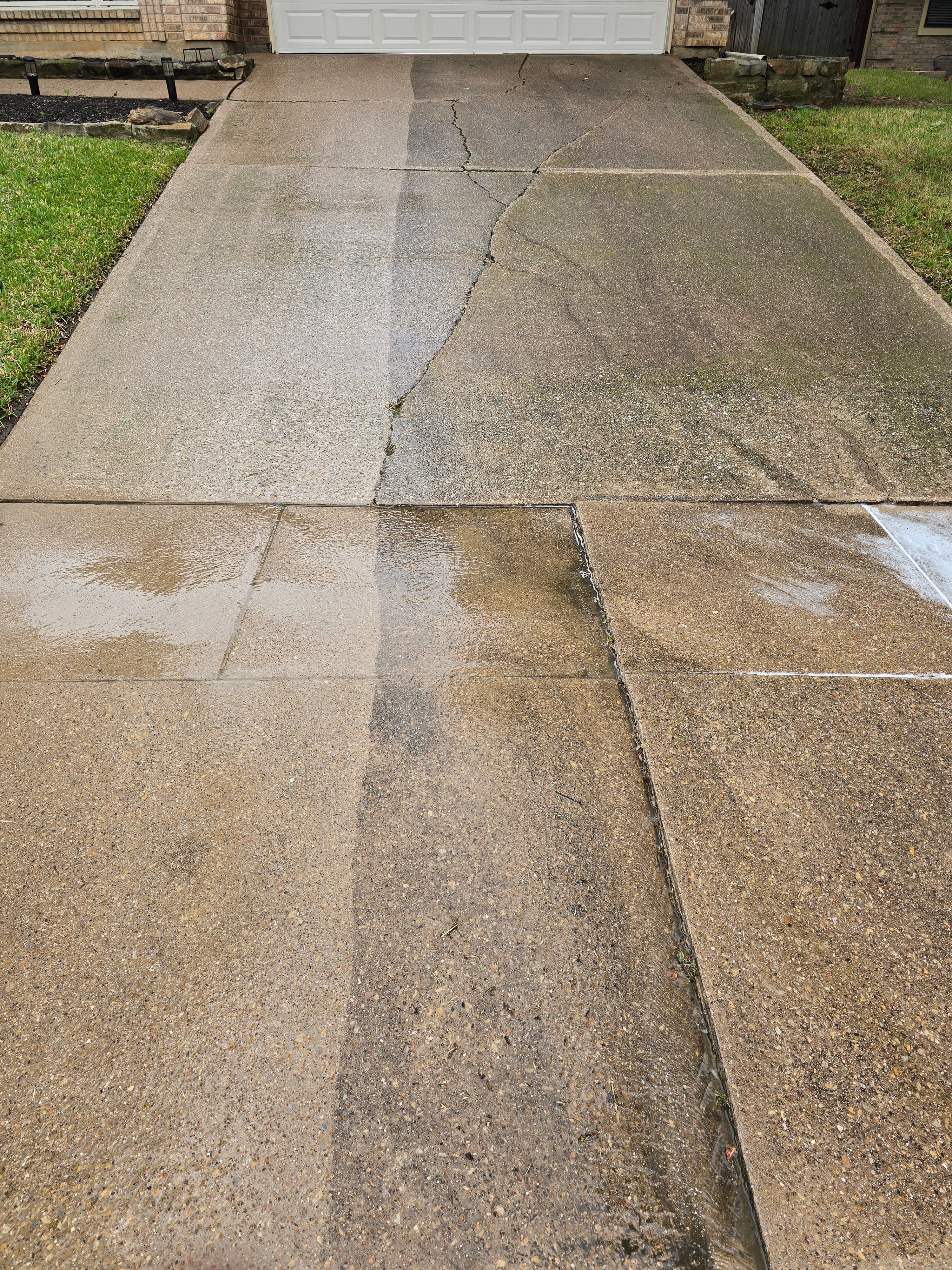 Wet cracked concrete driveway showing a stark contrast between the clean and dirty sections.