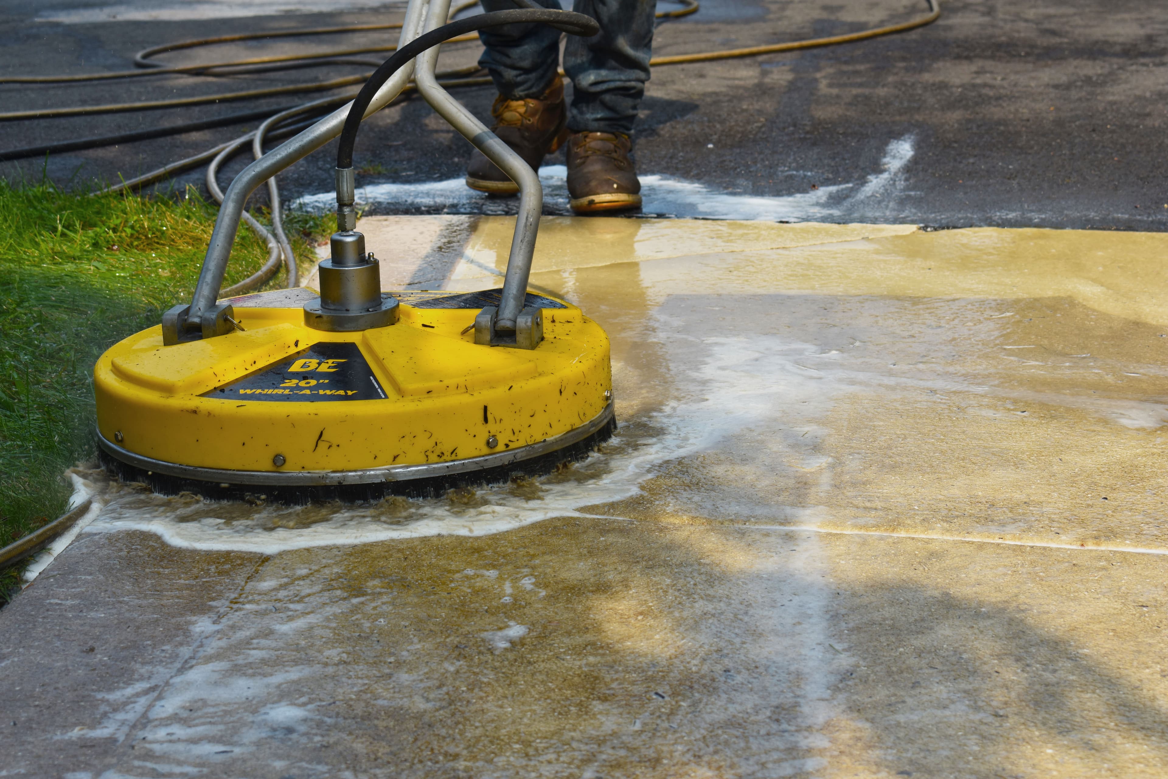 Yellow Whirl-A-Way surface cleaner pressure washing a dirty concrete sidewalk with soapy water.